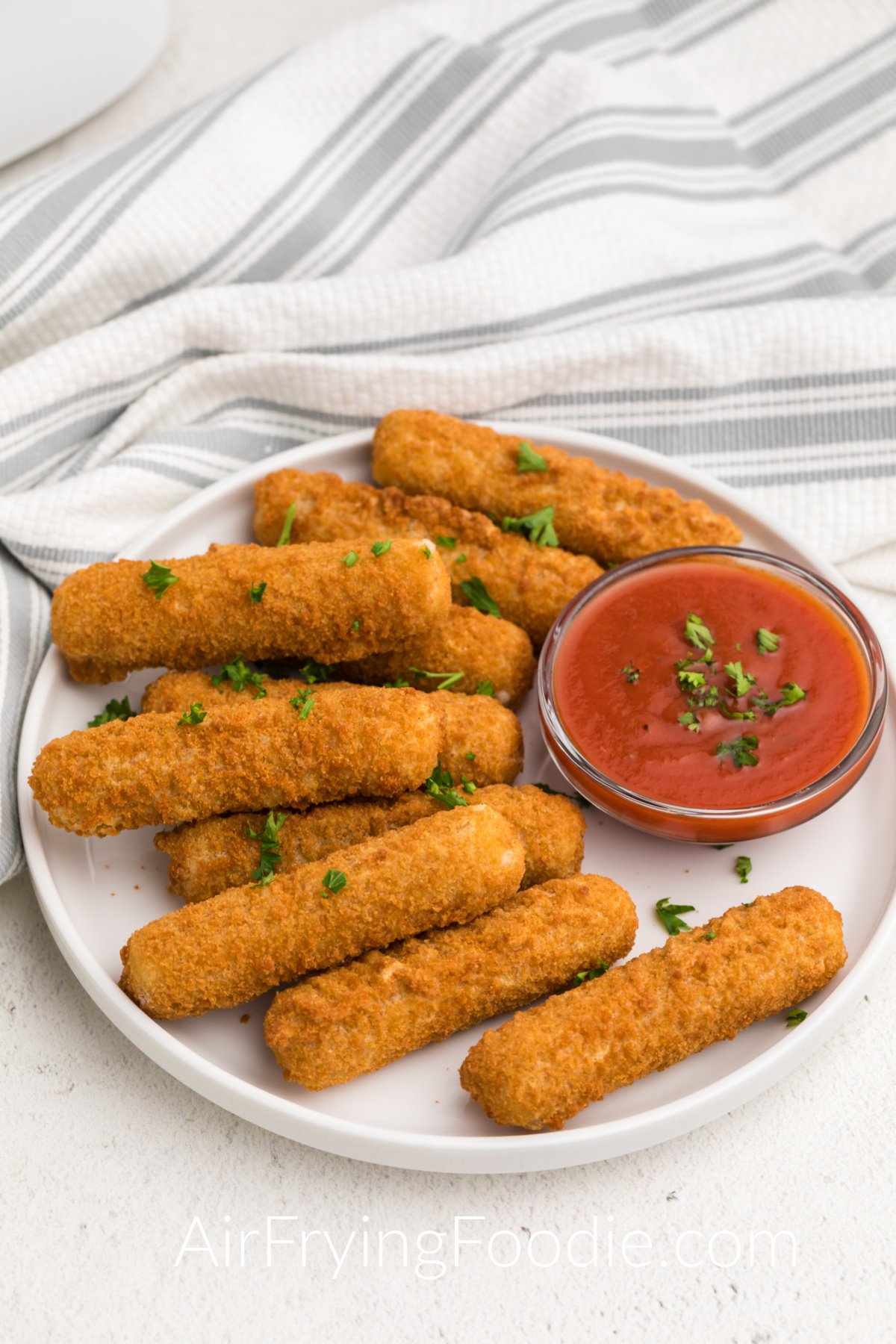 Air Fryer Mozzarella Sticks on a white plate with dipping sauce and topped with fresh parsley.