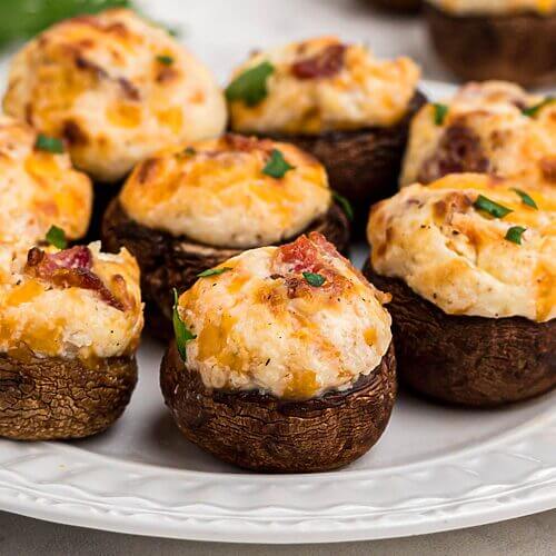 Brown mushroom caps stuffed with cream cheese, cheese, and bacon, and seasonings on a small white plate.