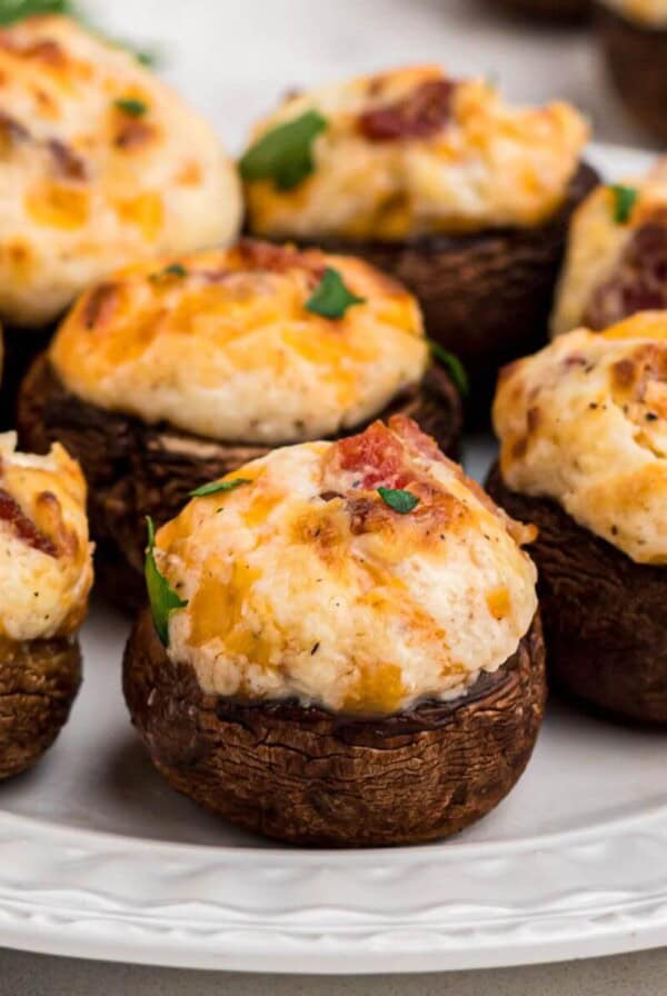 Brown mushroom caps stuffed with cream cheese, cheese, and bacon, and seasonings on a small white plate.