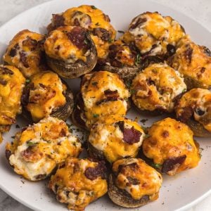 Cooked and cheesey stuffed mushrooms on a white plate after being cooked in the air fryer.