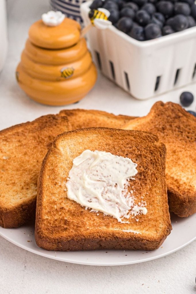 Golden toast on a white plate with honey and blueberries on the table