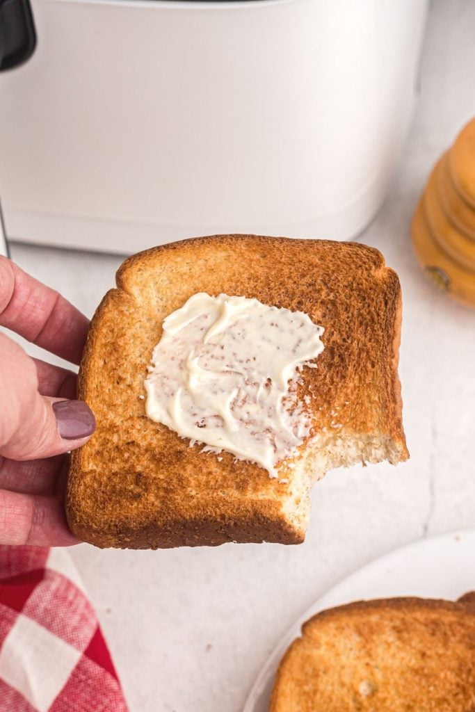 Golden slice of air fryer toast being held with a bite missing