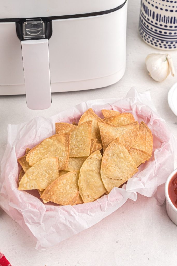 Golden tortilla chips in a basket with a bowl of salsa and cut limes on the table.