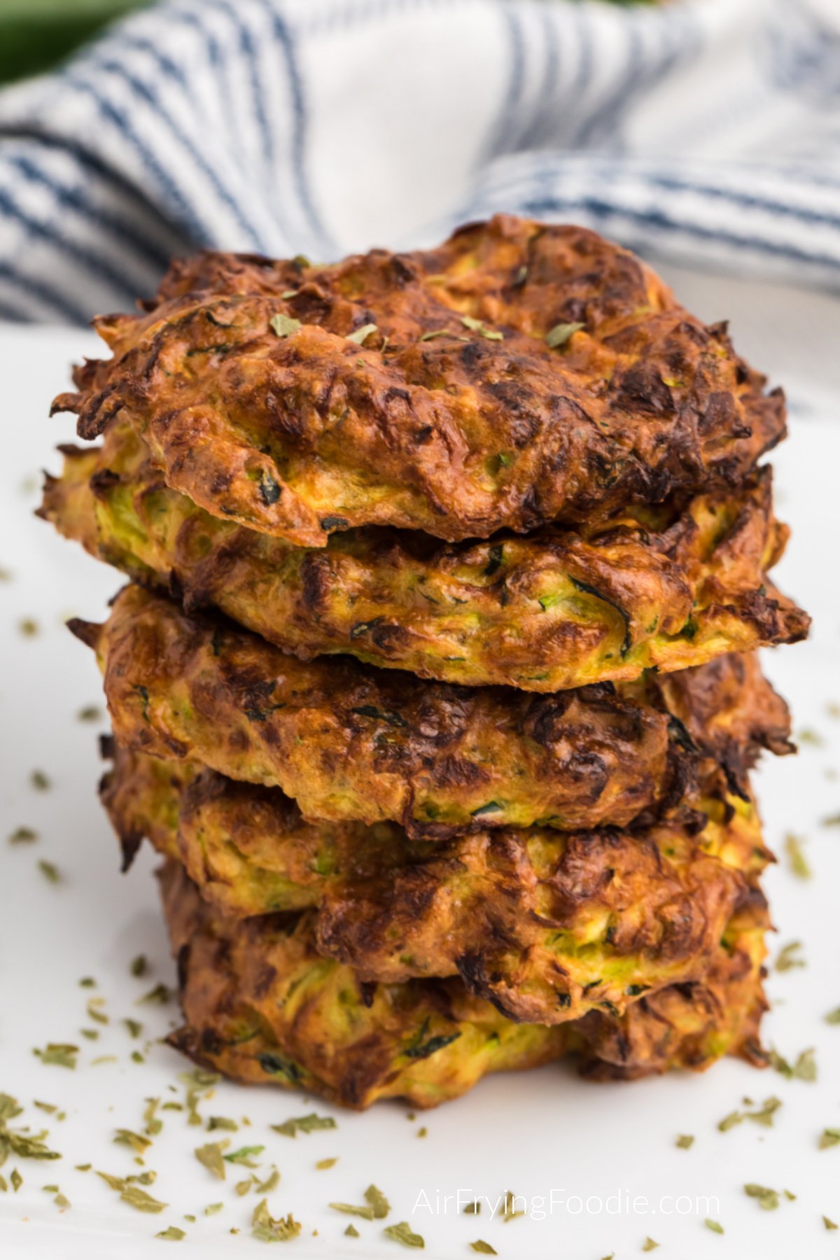 Zucchini fritters stacked on a plate and topped with parsley flakes. 