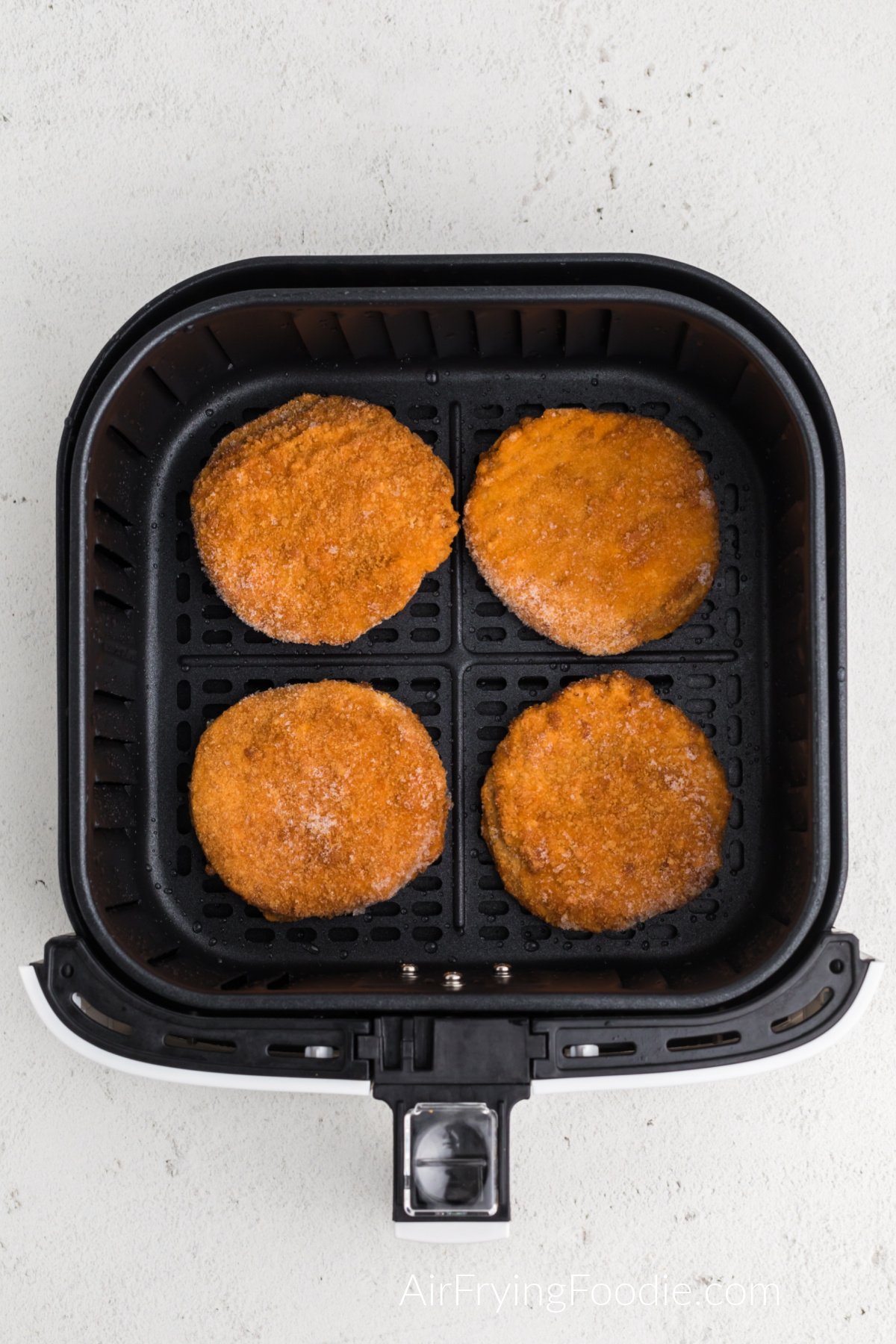 frozen chicken patties in air fryer basket ready to cook.
