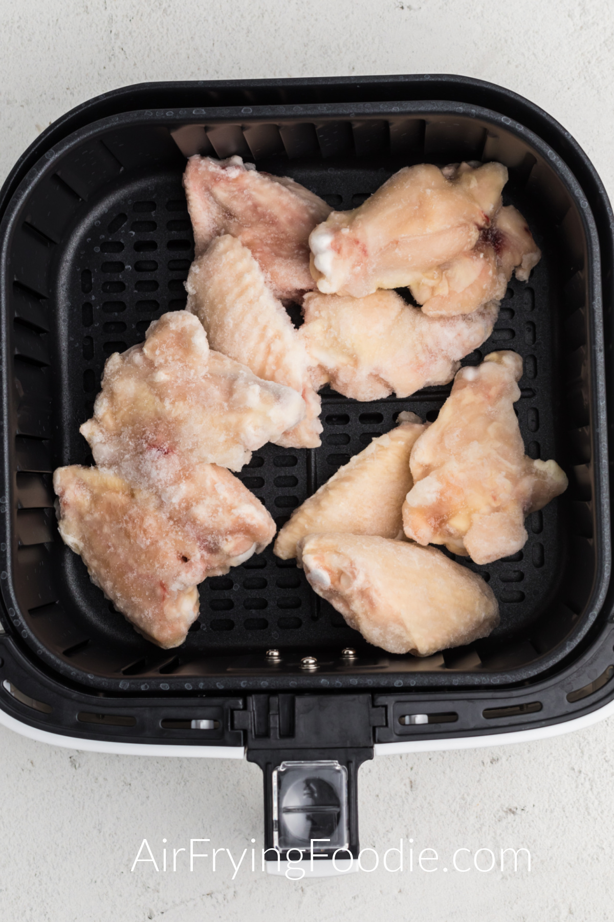 Frozen chicken wings in the basket of the air fryer.