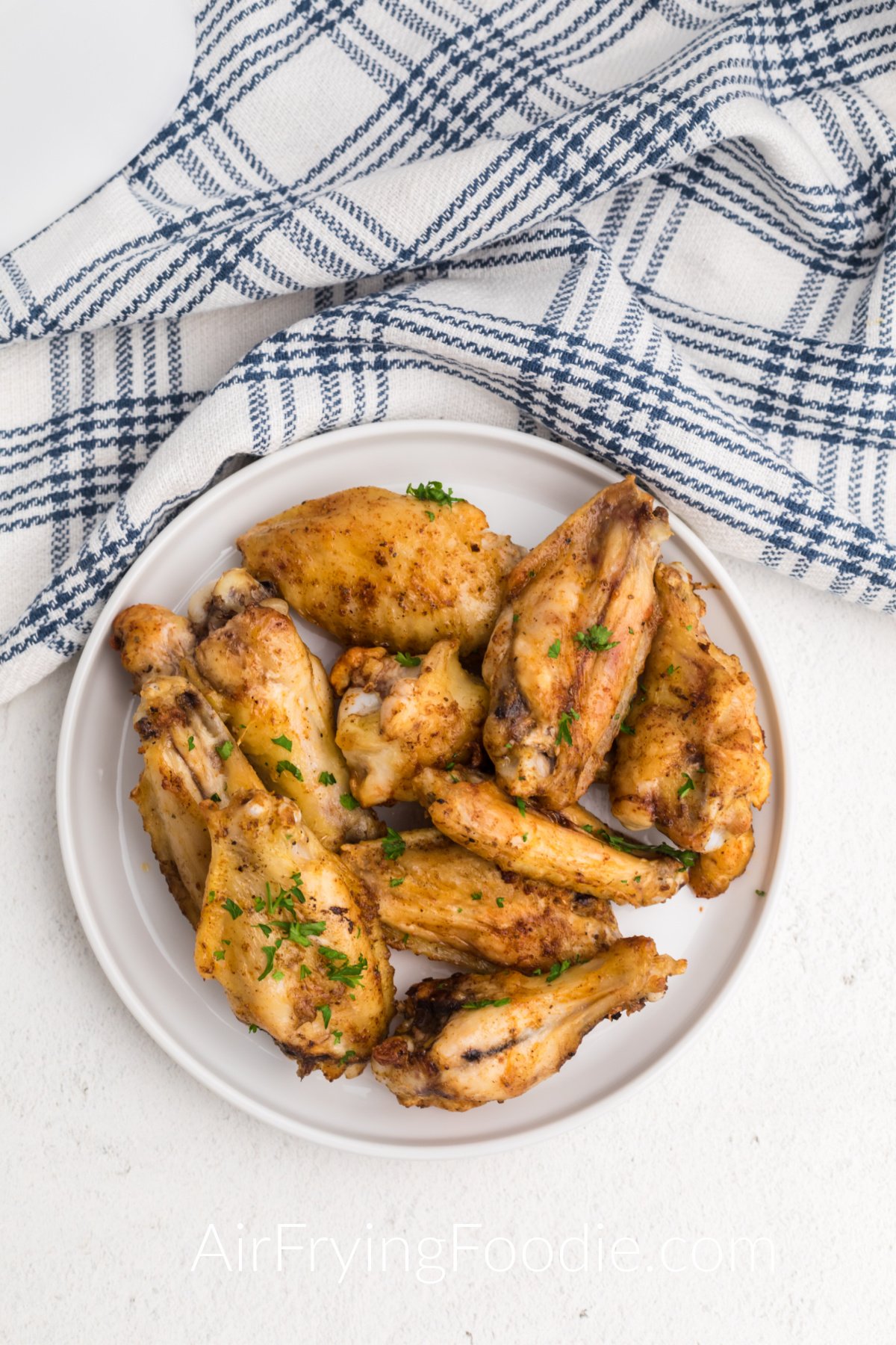Frozen chicken wings cooked and seasoned in the air fryer and served on a white plate. 