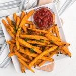 Frozen sweet potato fries made in the air fryer - fully cooked and served on a white plate with a side of ketchup.