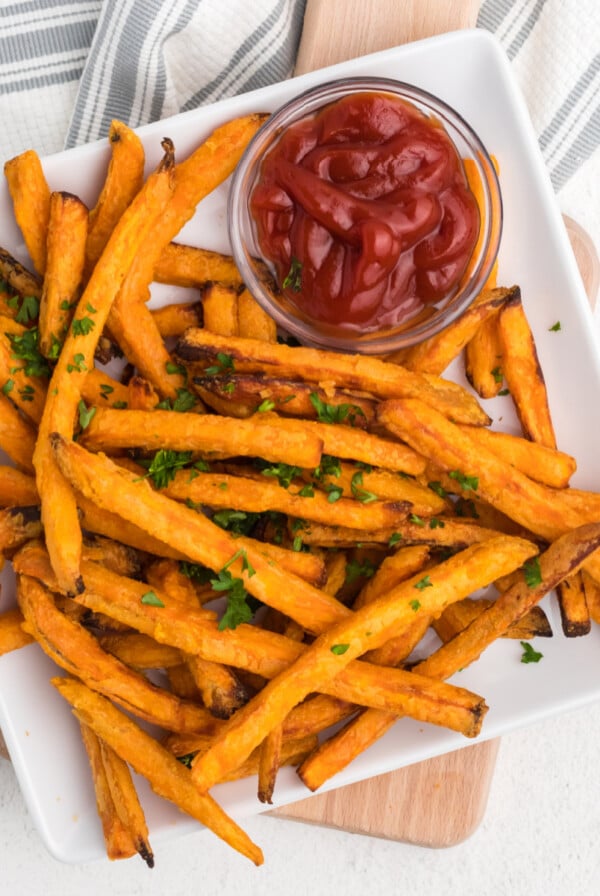 Frozen sweet potato fries made in the air fryer - fully cooked and served on a white plate with a side of ketchup.