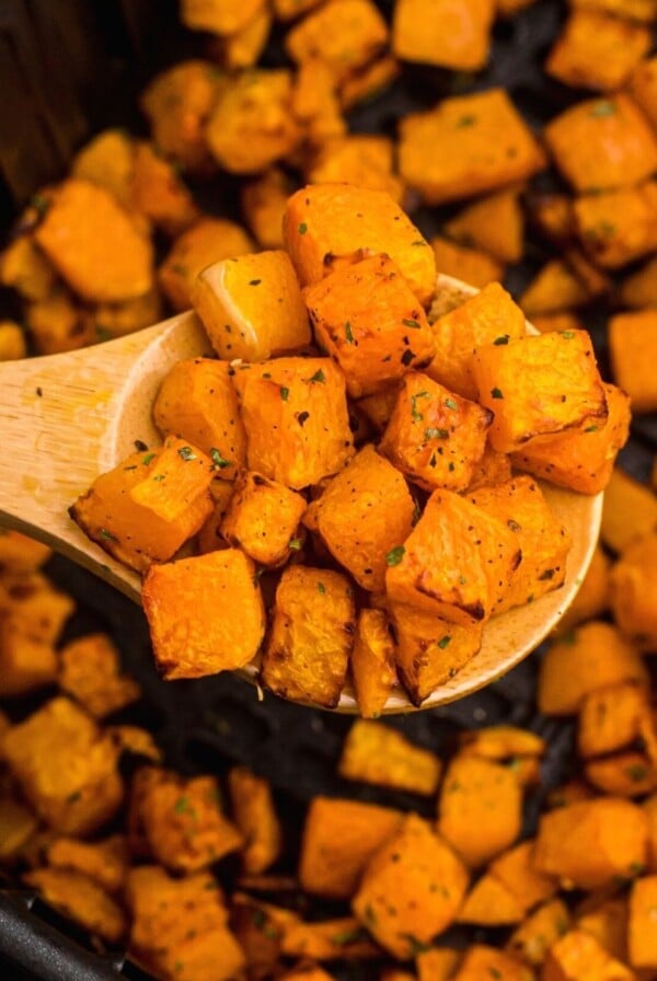 Wooden spoon with cooked squash over the air fryer basket.