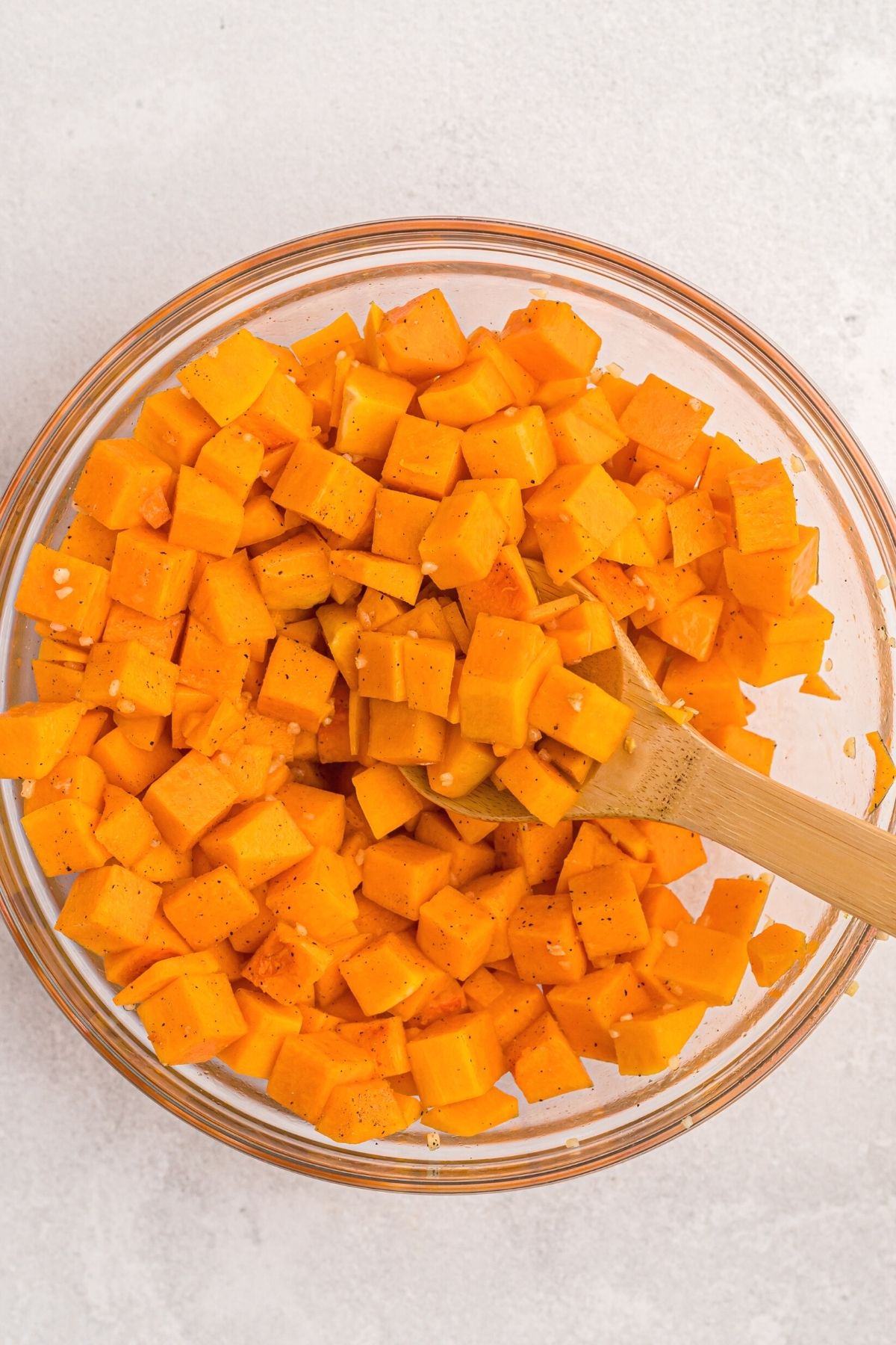Orange butternut squash in a glass bowl being mixed with seasonings with a wooden spoon