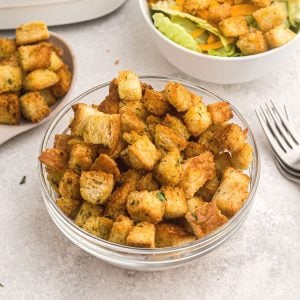 Clear glass bowl of golden croutons in front of a bowl of salad