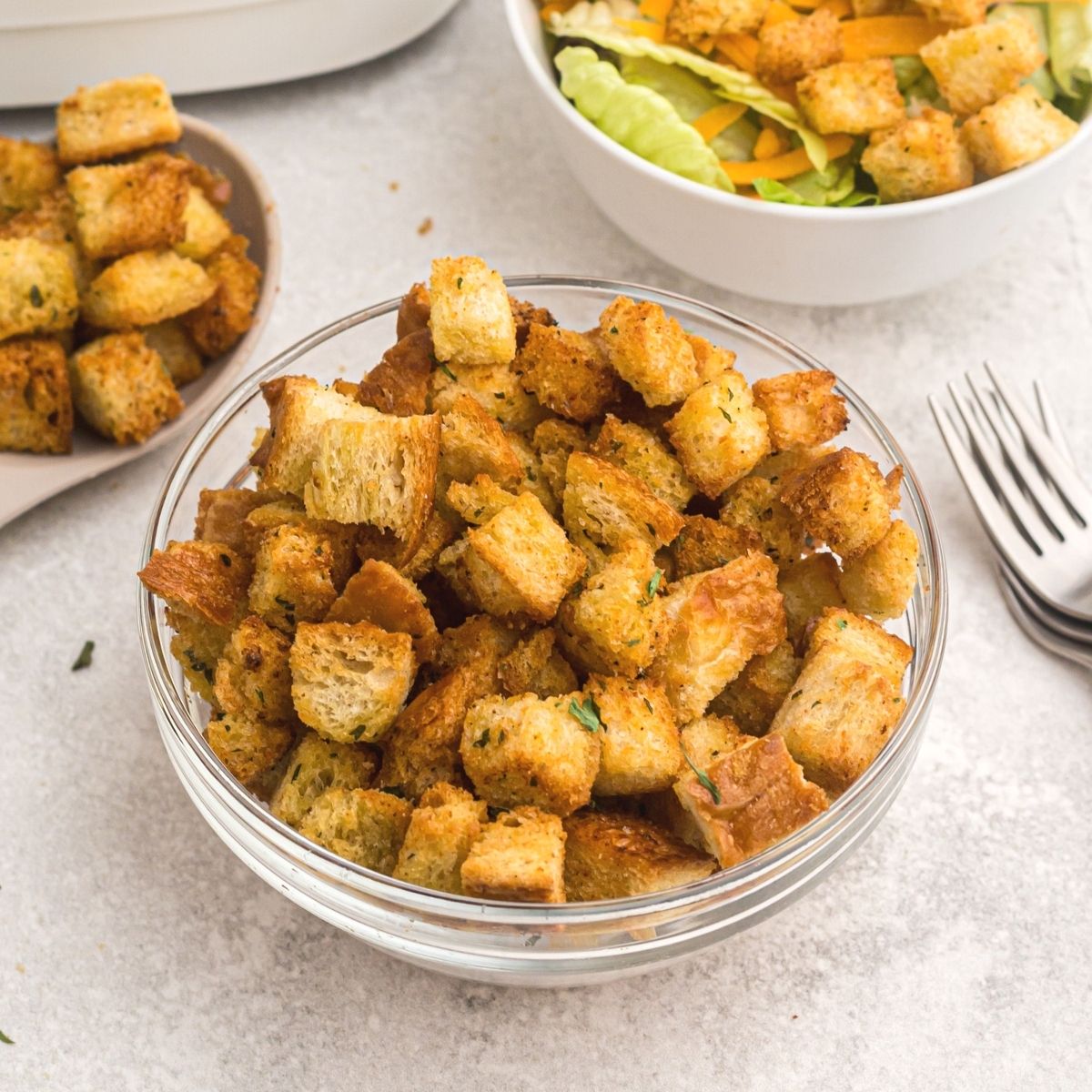 Clear glass bowl of golden croutons in front of a bowl of salad