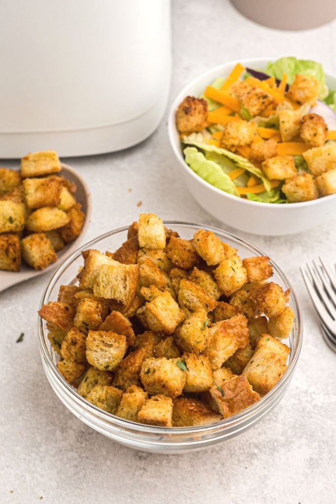 Golden crispy croutons seasoned in a glass bowl in front of a salad