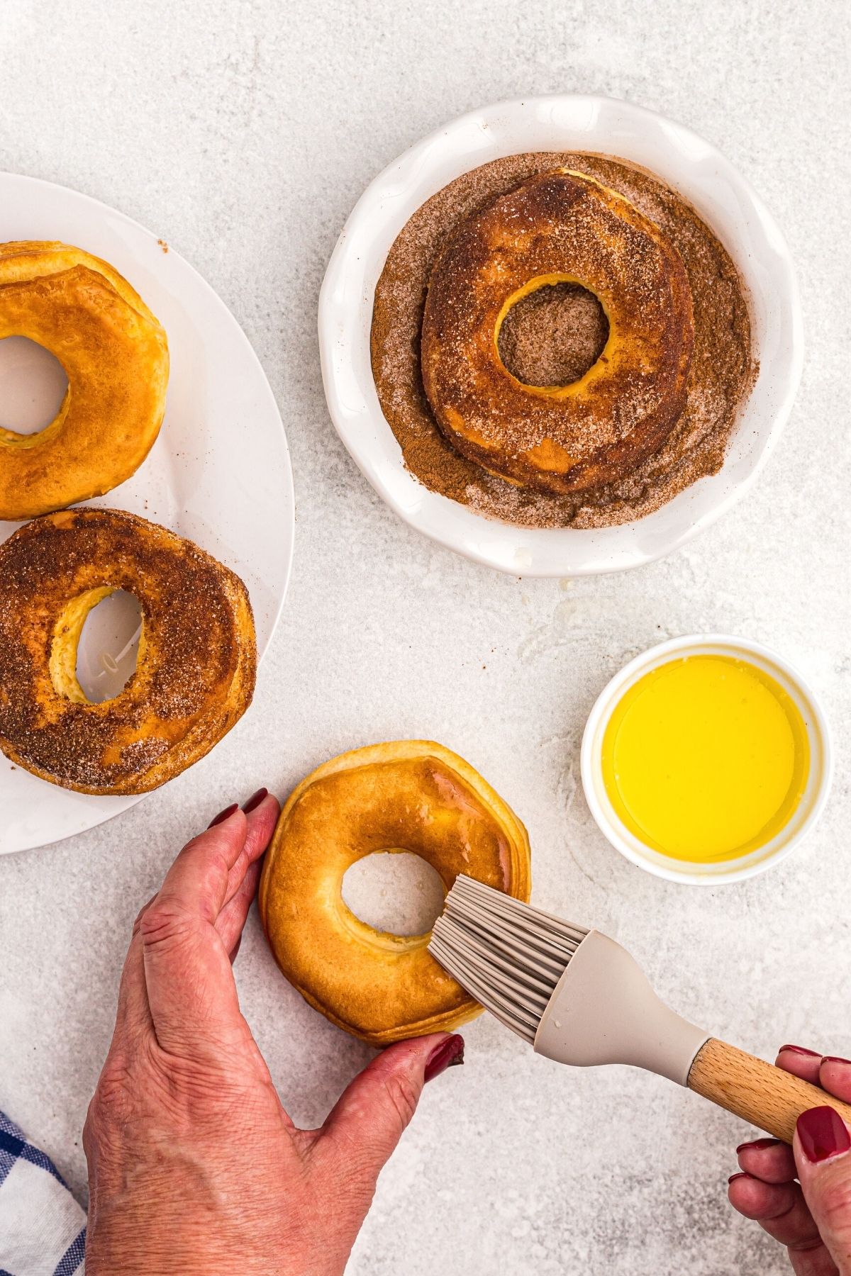 brushing donuts with melted butter before dipping into cinnamon and sugar coating