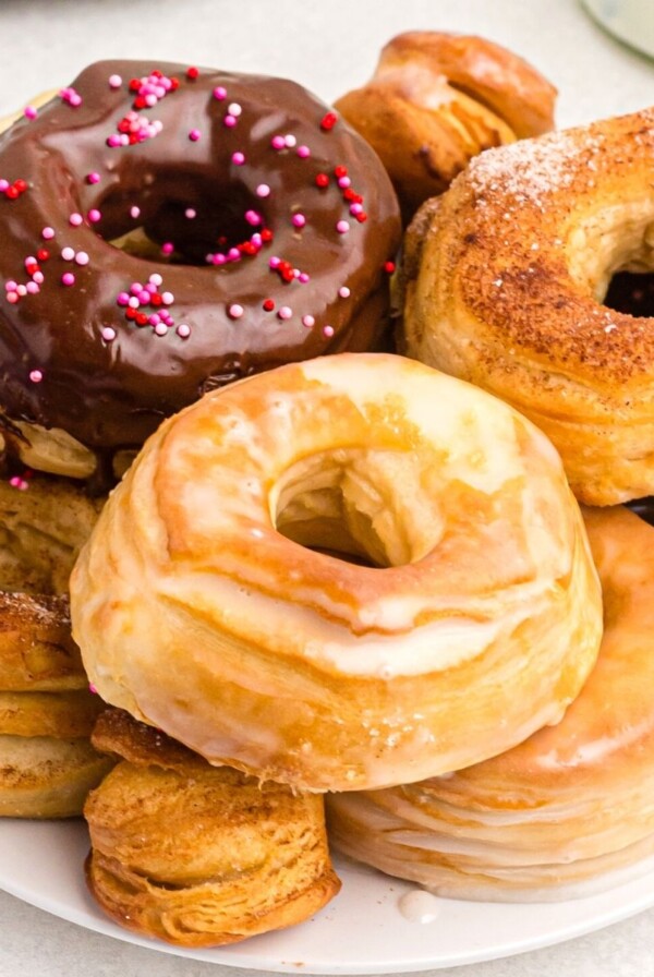 Plate of glazed, sugar coated, and chocolate covered golden donuts on a white plate served on a white marble table.