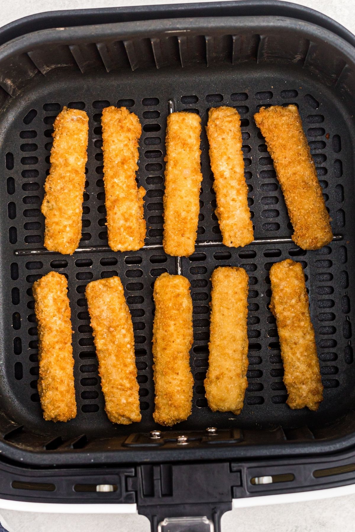 Golden fish sticks before being fried in an air fryer basket