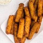 Golden fish sticks stacked on a white plate with a side of tartar sauce