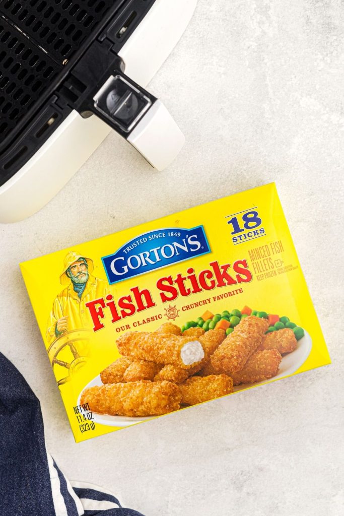 Box of Gorton's Fish Sticks on a white marble table with an air fryer basket. 