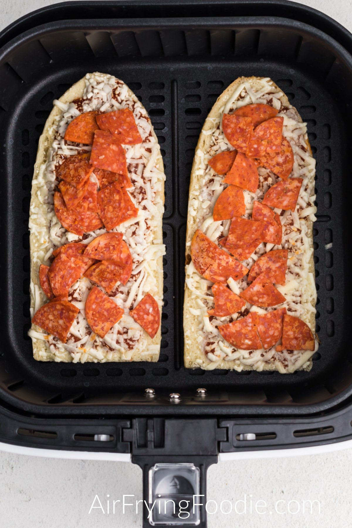 Frozen french bread pizzas in the basket of the air fryer.