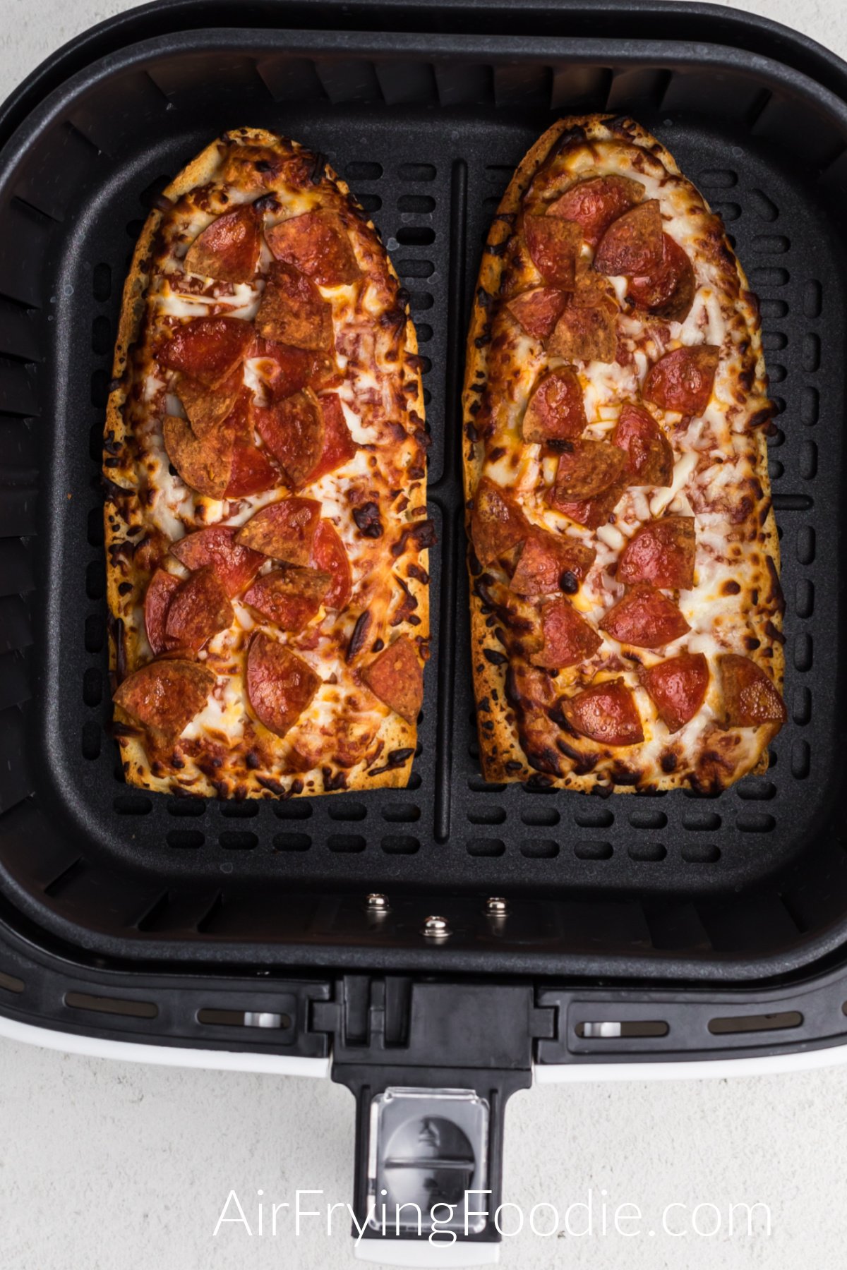Air fried french bread pizzas in the basket of the air fryer. 