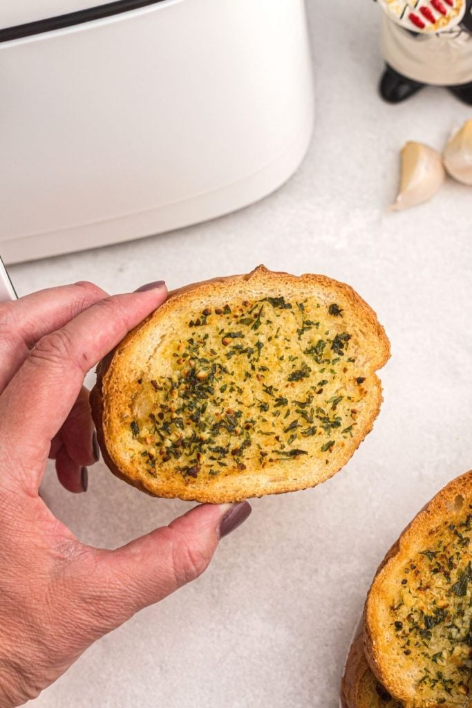 Golden garlic bread slice being held in front of an air fryer