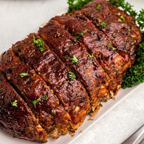 Juicy meatloaf sliced on a white plate sprinkled with parsley flakes