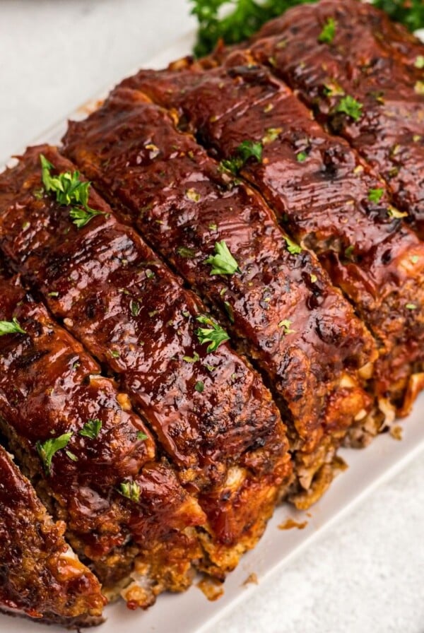 Juicy meatloaf sliced on a white plate sprinkled with parsley flakes