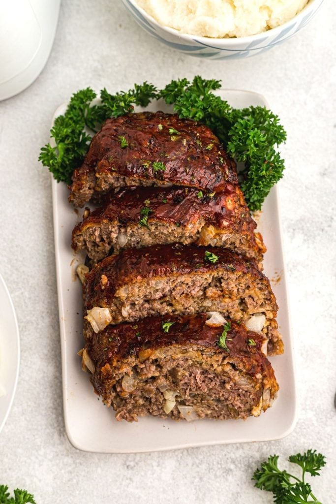 Golden brown meatloaf on a white square plate with parsley garnish.