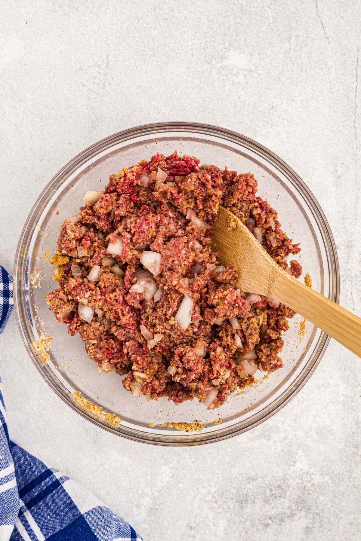 Ground beef being mixed with seasonings, onions, and breadcrumbs