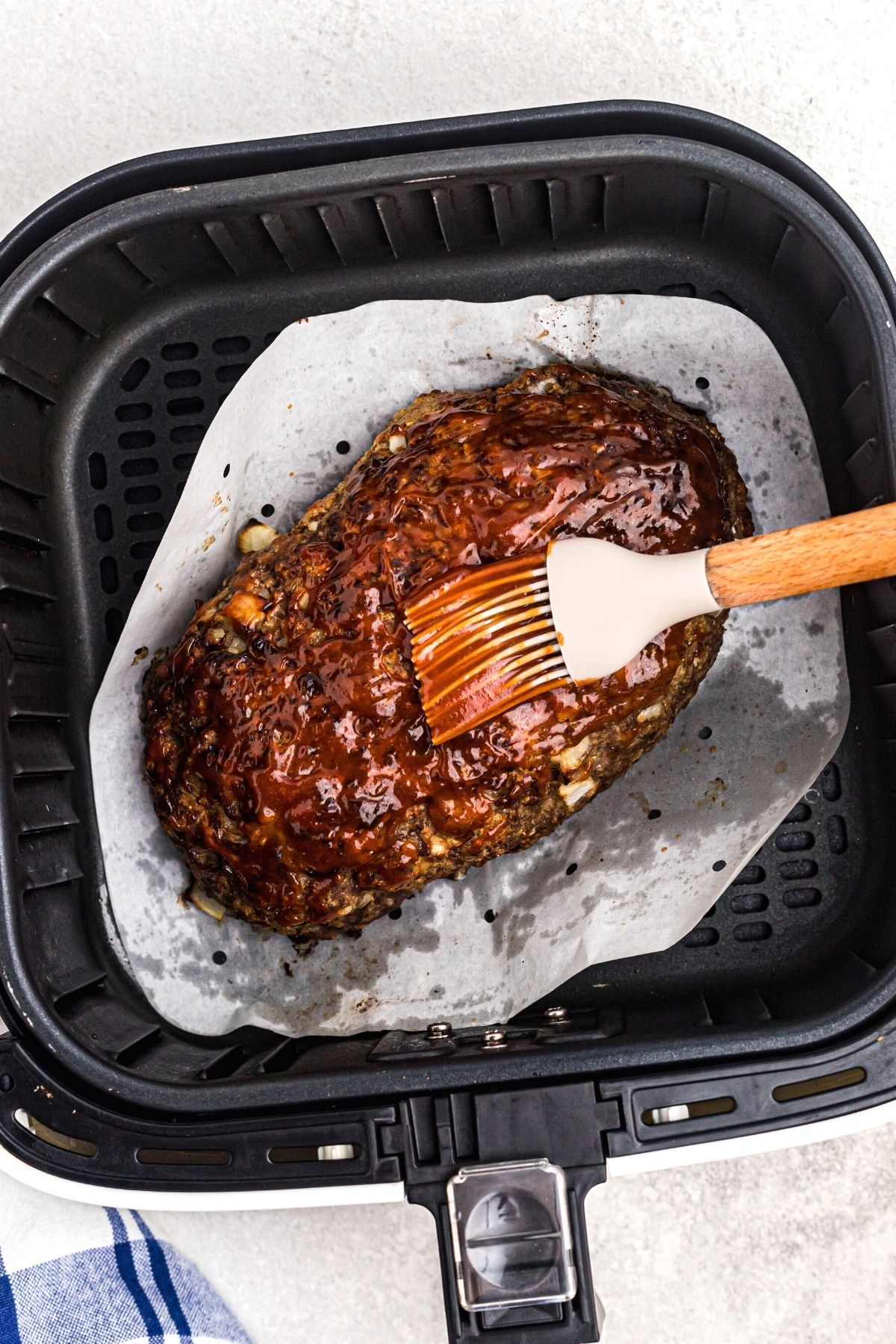 Brushing sauce to top meatloaf in the air fryer basket.