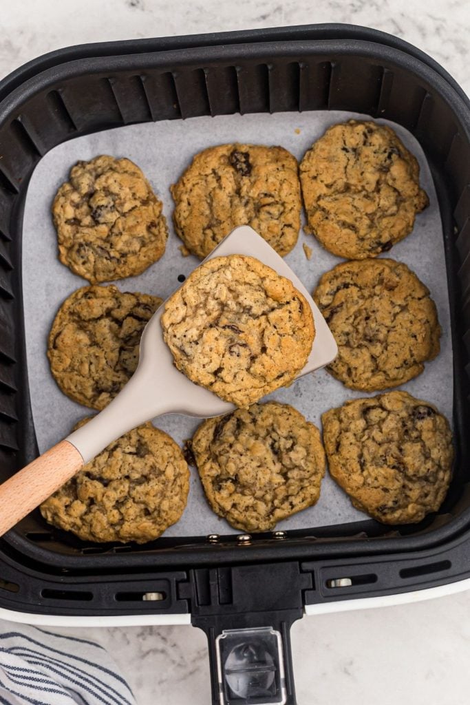 Golden oatmeal raisin cookies being lifted on a spatula out of the air fryer basket