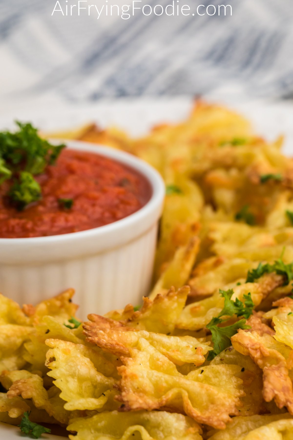 Close up shot of air fried pasta chips in a white plate with a side of marinara sauce.