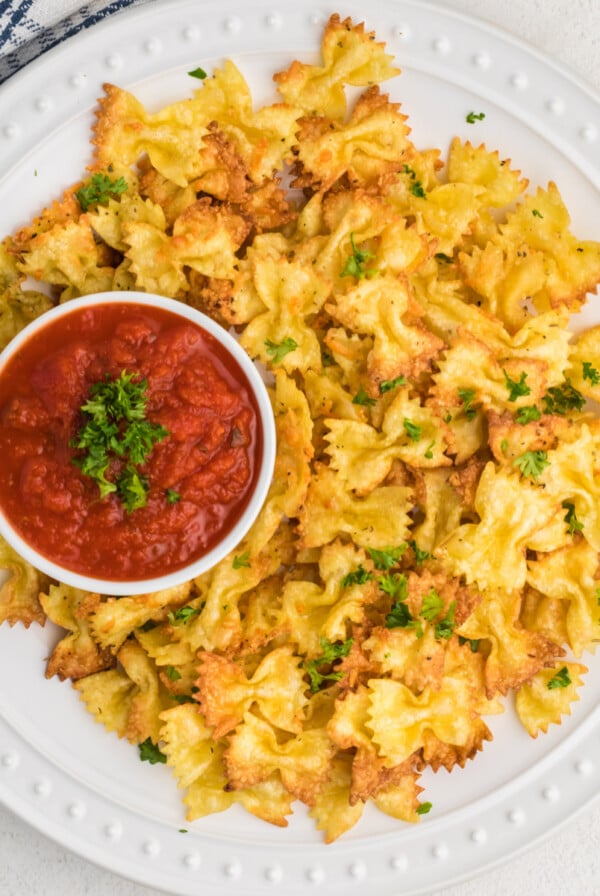 Overhead shot of air fried bow tie pasta chips with a side or marinara sauce.