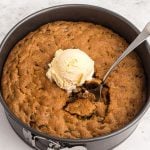 Golden cookie in a pan after being cooked in air fryer. Topped with vanilla ice cream and a spoon taking a scoop bit.
