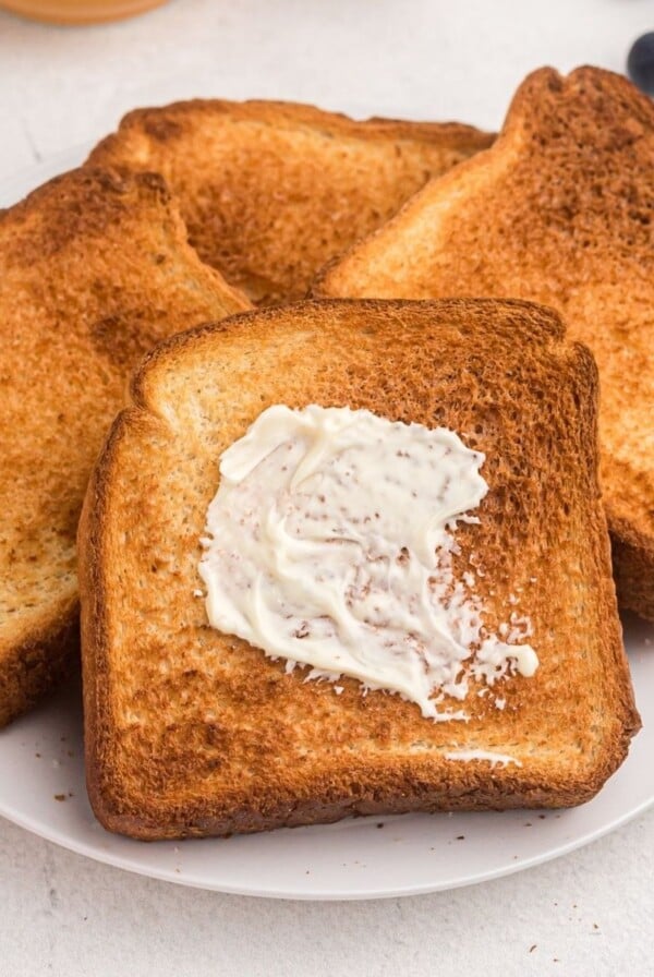 Golden toast with one being buttered. Served on a white plate with blueberries and butter.