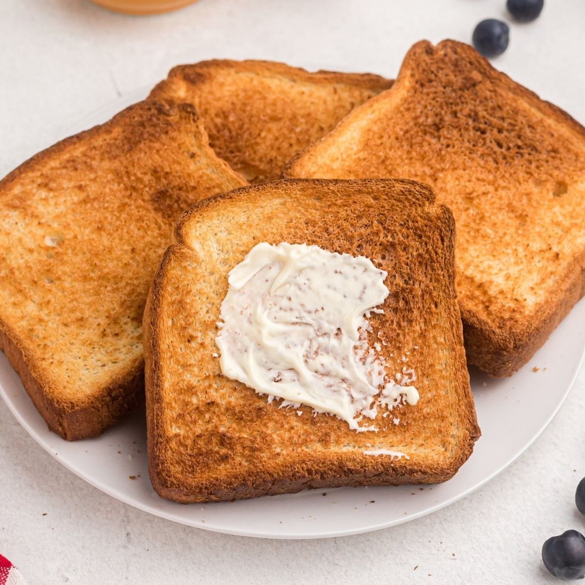 Golden toast with one being buttered. Served on a white plate with blueberries and butter.