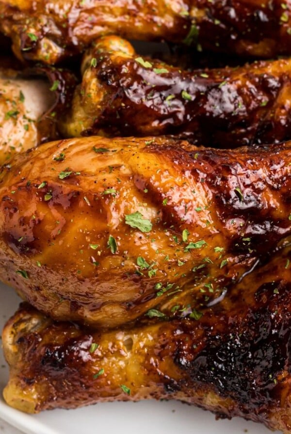 Juicy BBQ coated chicken on a white plate garnished with parsley flakes