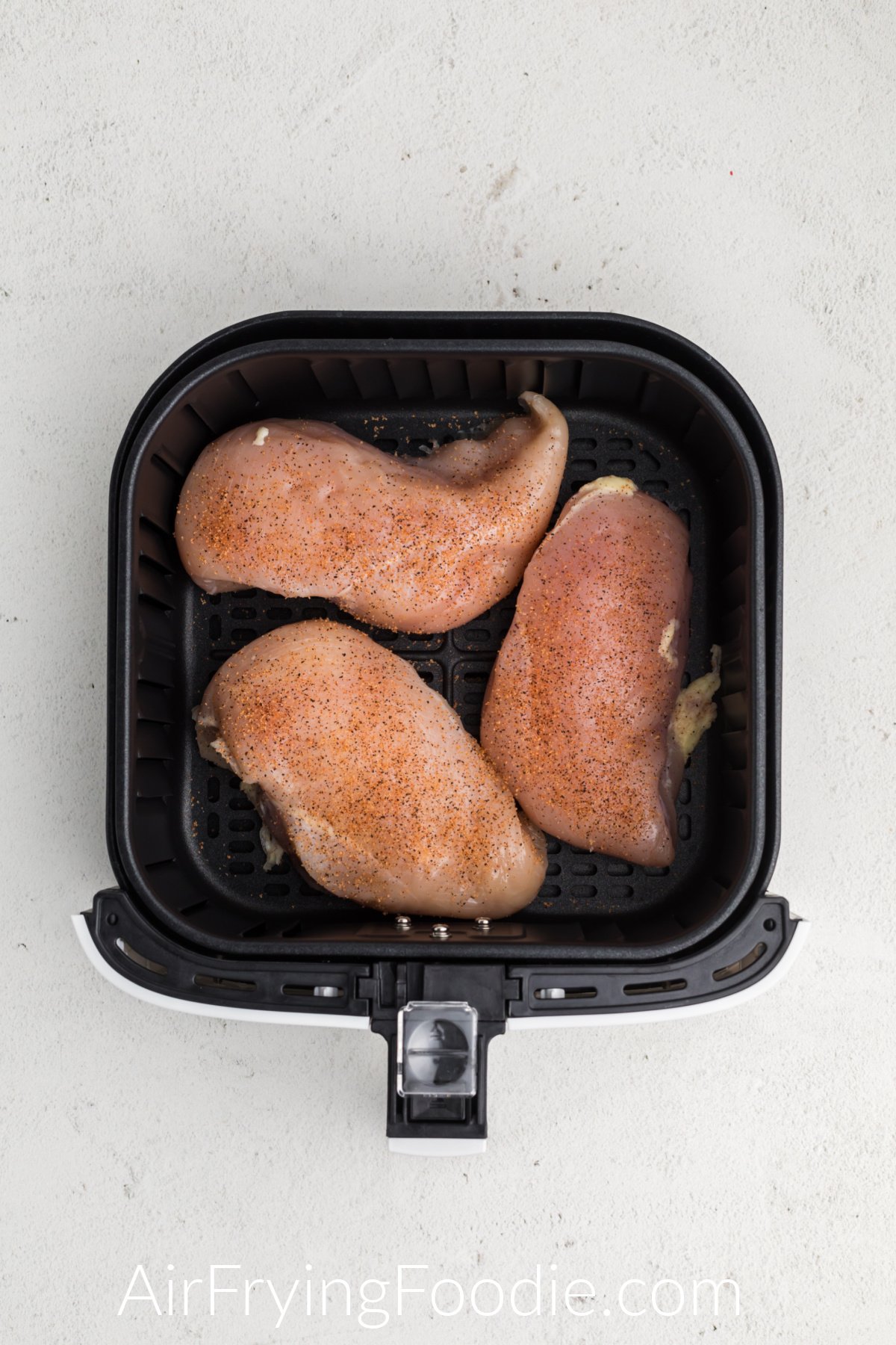 frozen chicken breasts seasoned and placed in a single later in the air fryer basket.
