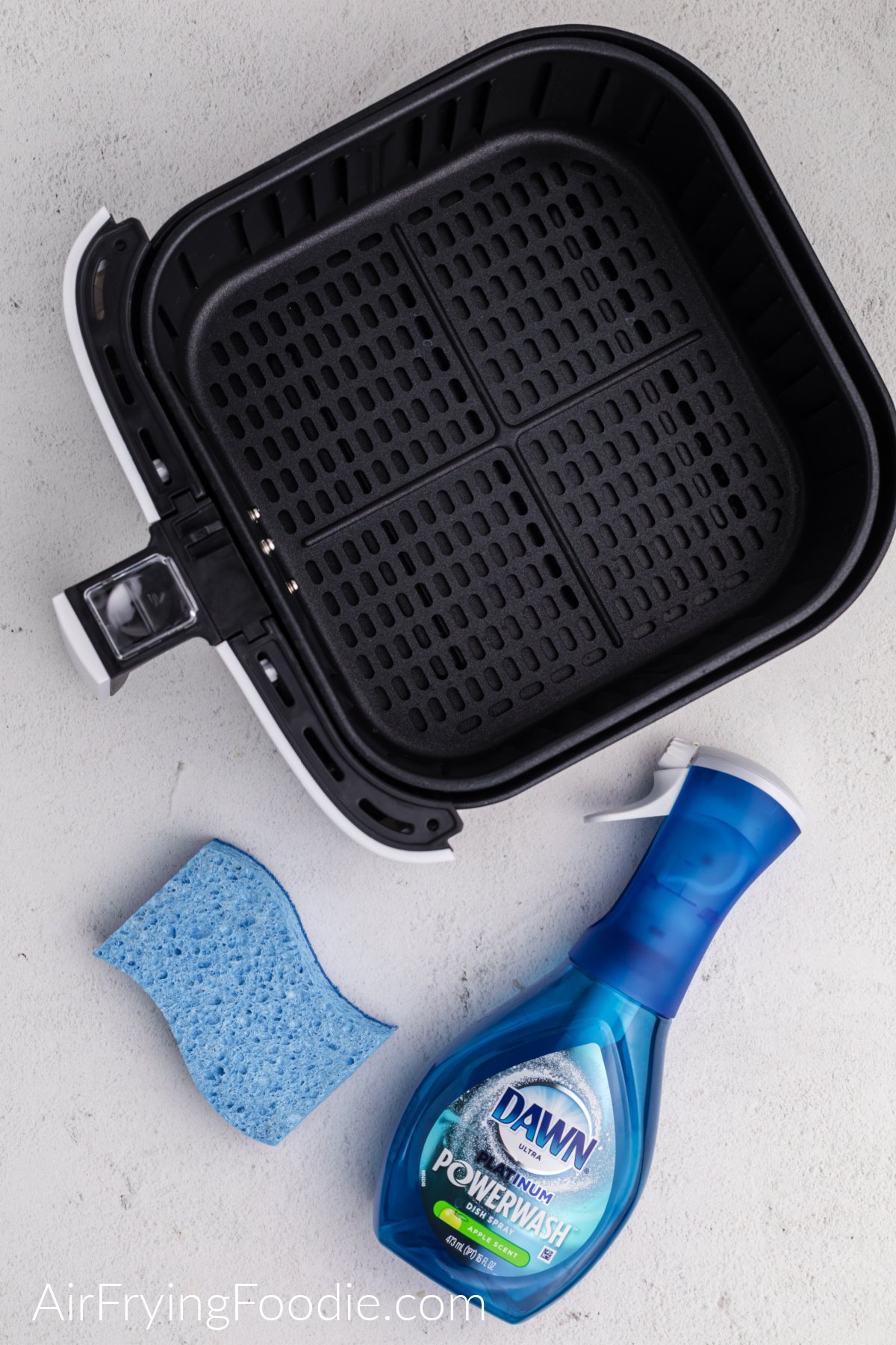 Air fryer basket, sponge, and Dawn powerwash on a white table. 