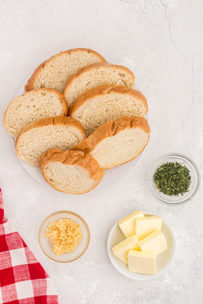 Ingredients to make garlic bread, bread, butter, garlic, parsley flakes