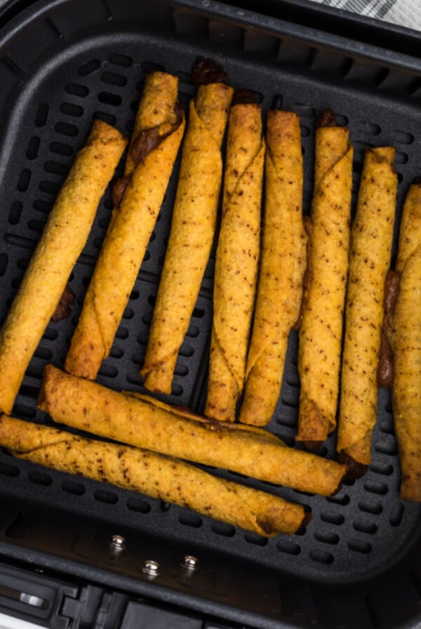 fully cooked taquitos in the air fryer basket in a single layer, ready to be removed and served.