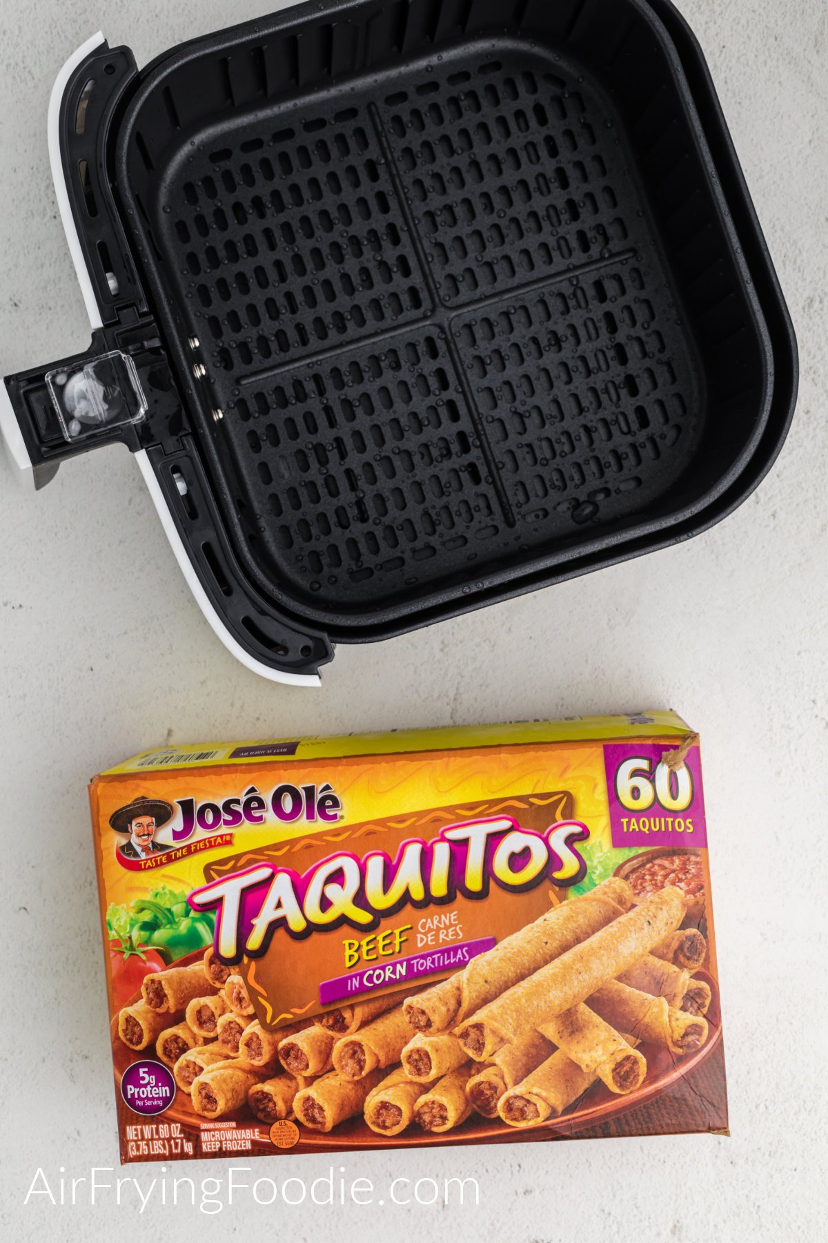 Box of frozen Jose Ole taquitos and an air fryer basket on a white table. 