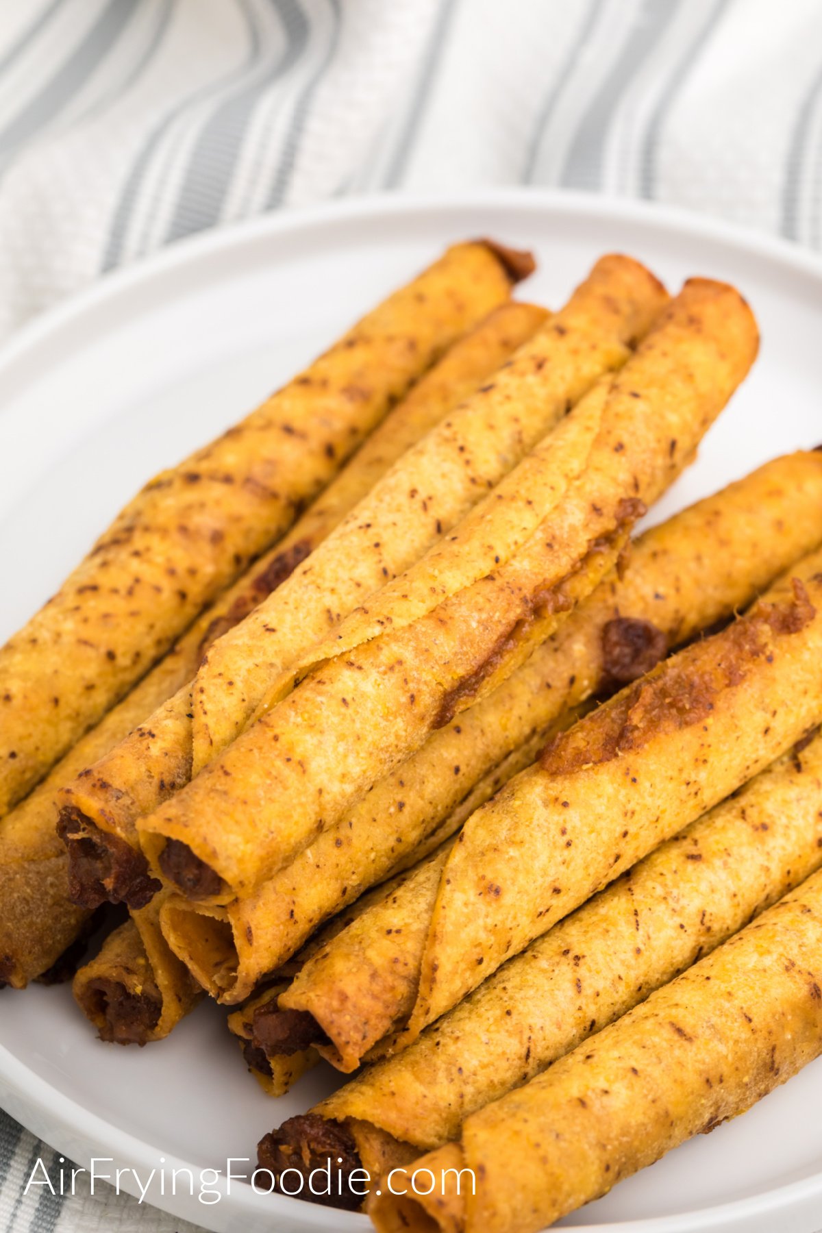 Taquitos cooked in the air fryer from frozen and served on a white plate. 