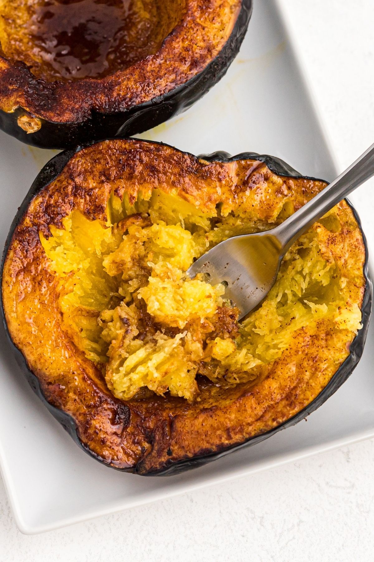 Golden cooked acorn squash on a white plate with a fork bite in the center of the squash.