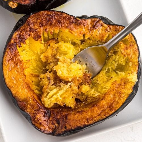 Golden brown acorn squash being scooped with a fork on a white plate
