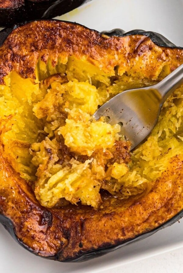 Golden brown acorn squash being scooped with a fork on a white plate