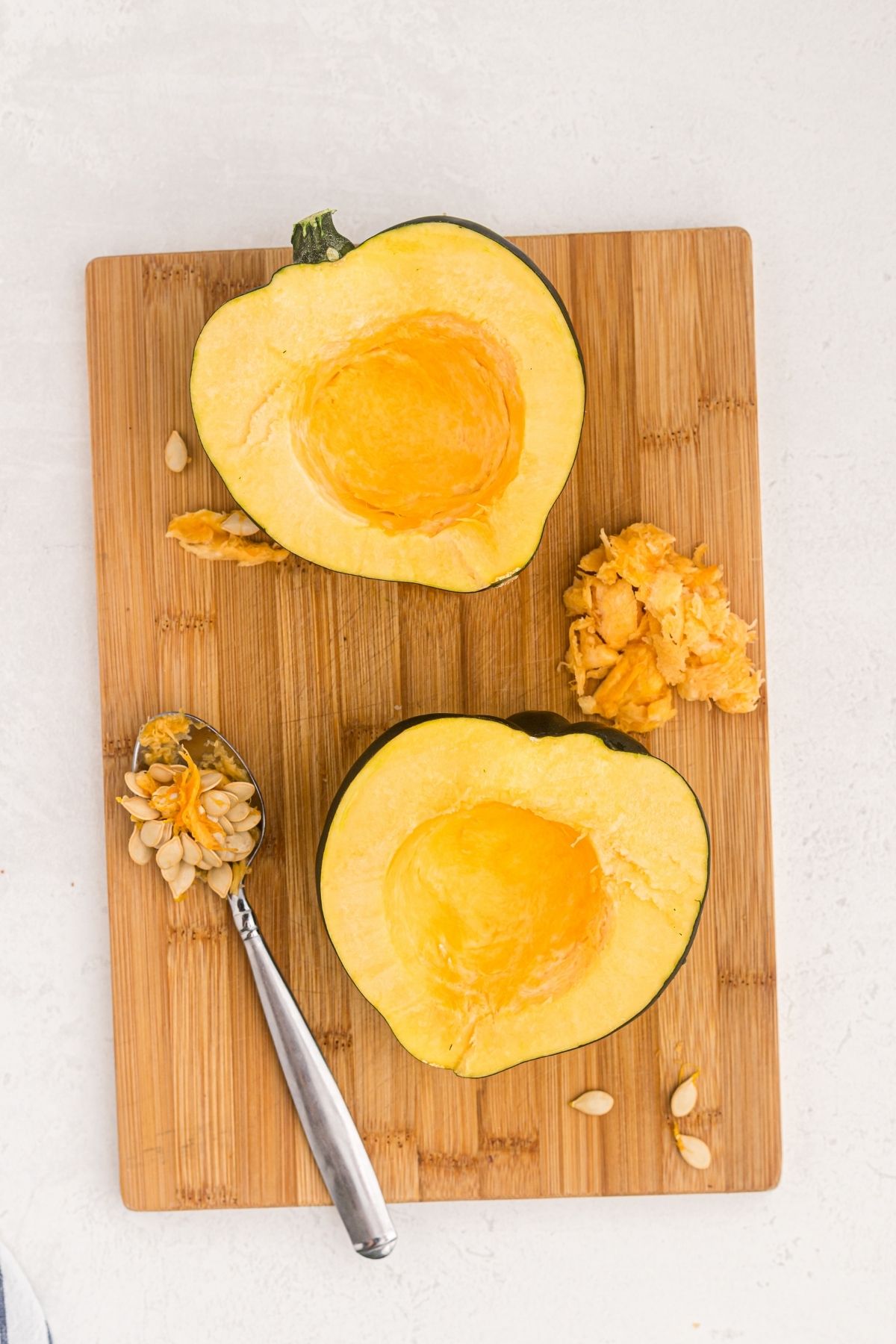 Acorn squash cut in half with a spoon scooping out seeds on a wooden cutting board