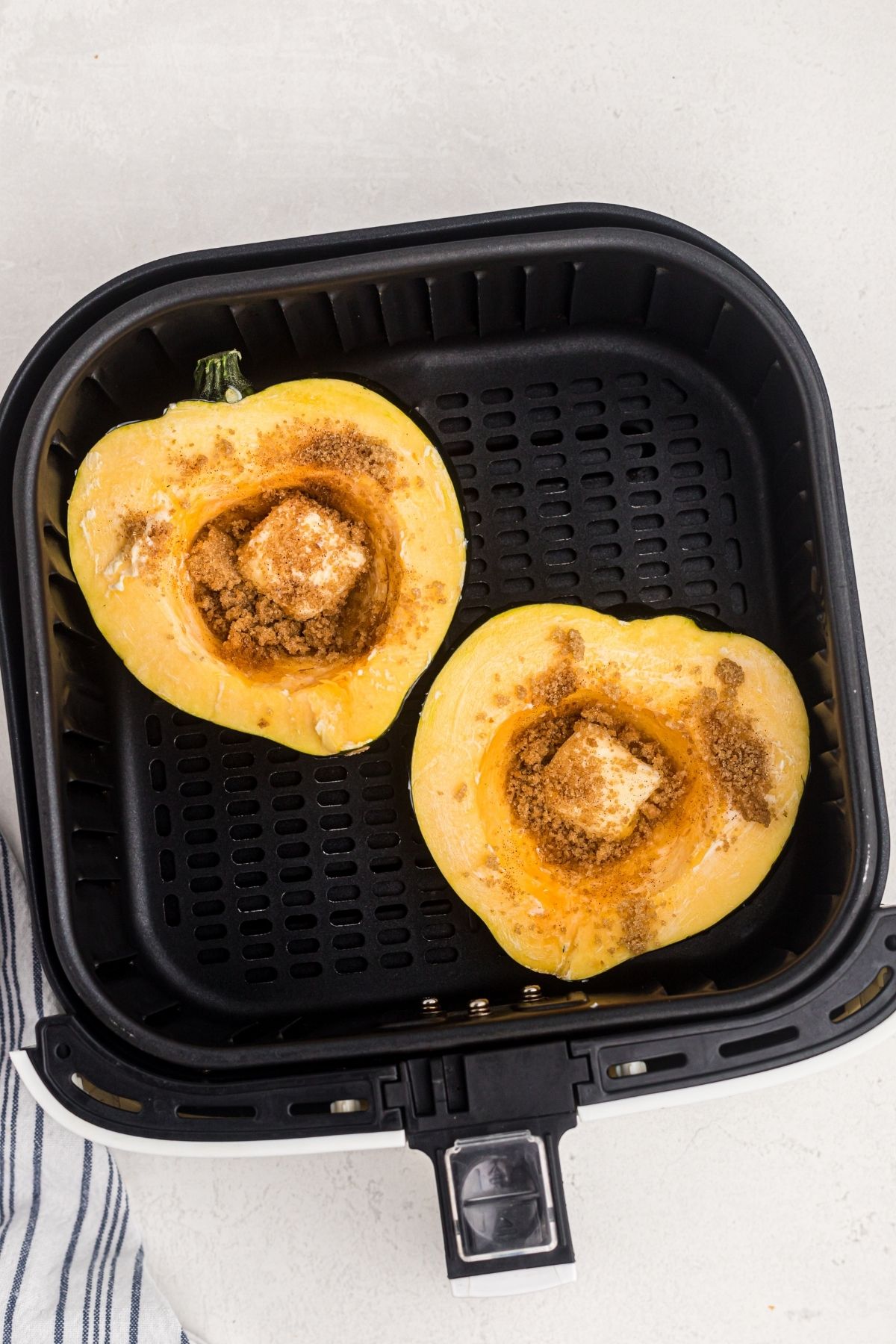 Acorn squash sliced in half filled with butter and brown sugar mixture in the air fryer basket before being cooked