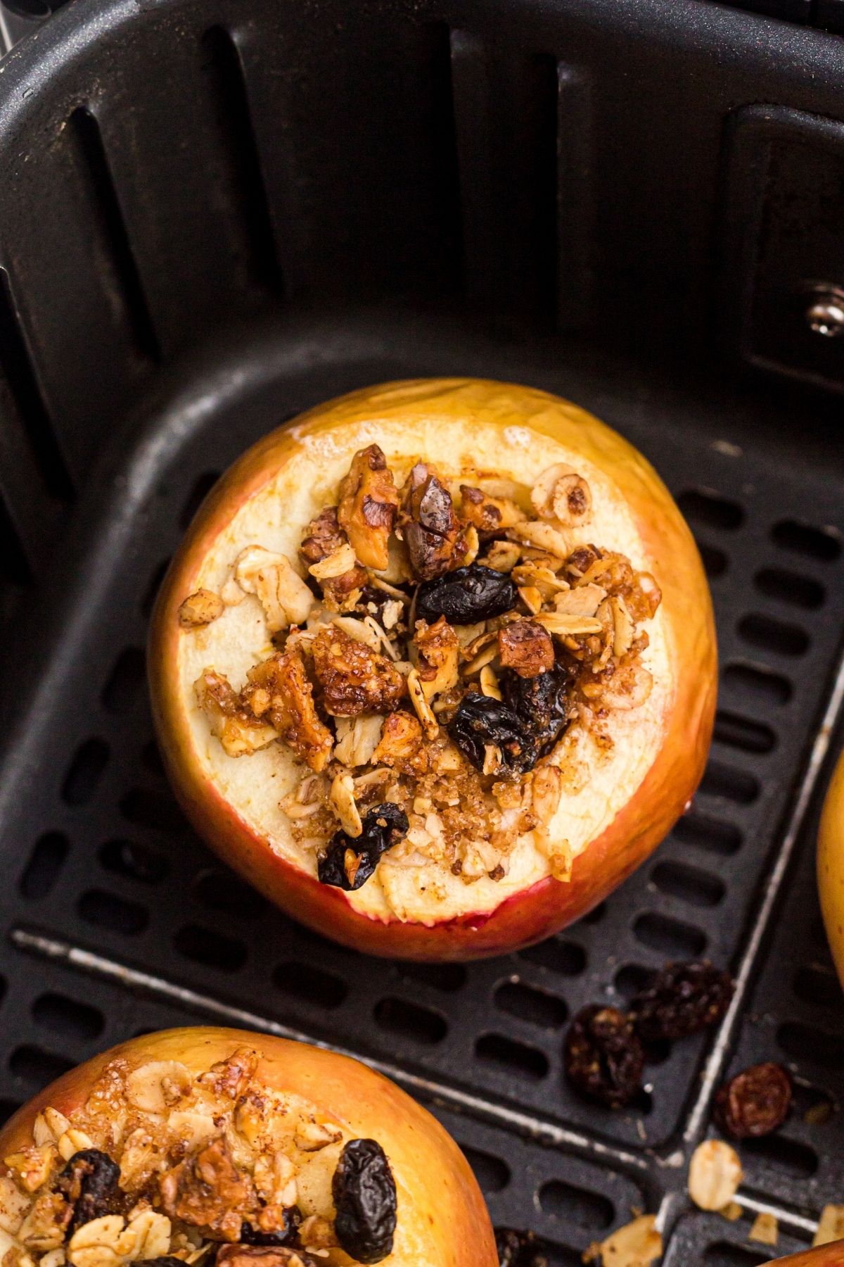 Baked apples stuffed with oats, cranberries, sugar, and butter, and in the basket of an air fryer.